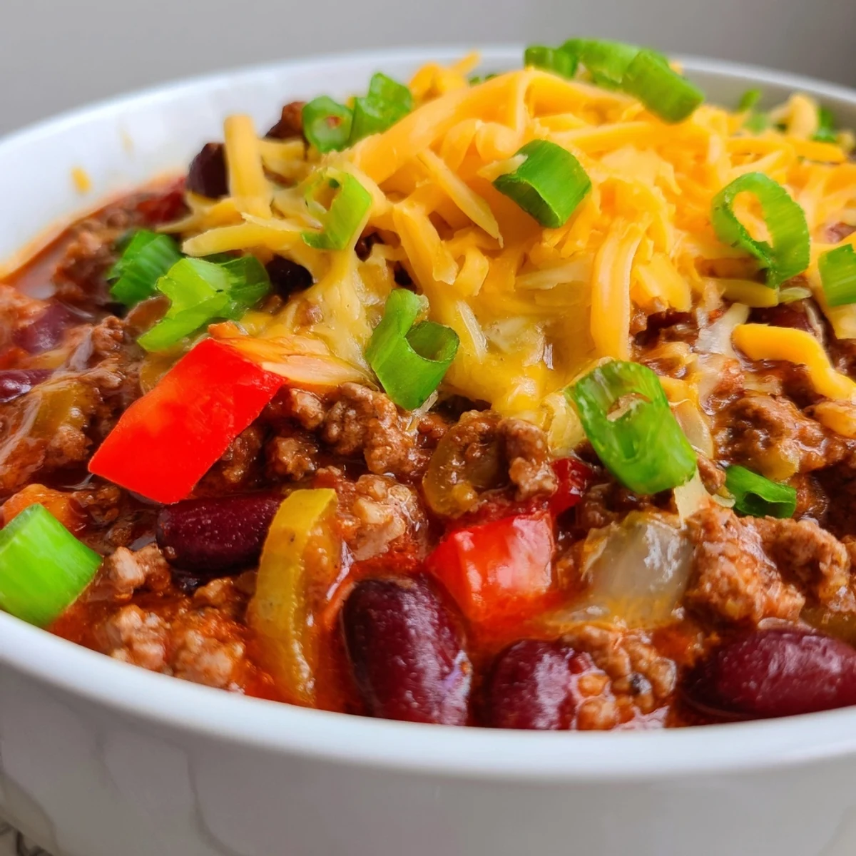 Golden melted sharp cheddar topping Beef and Bean Chili in a rustic pot, garnished with jalapeño slices.