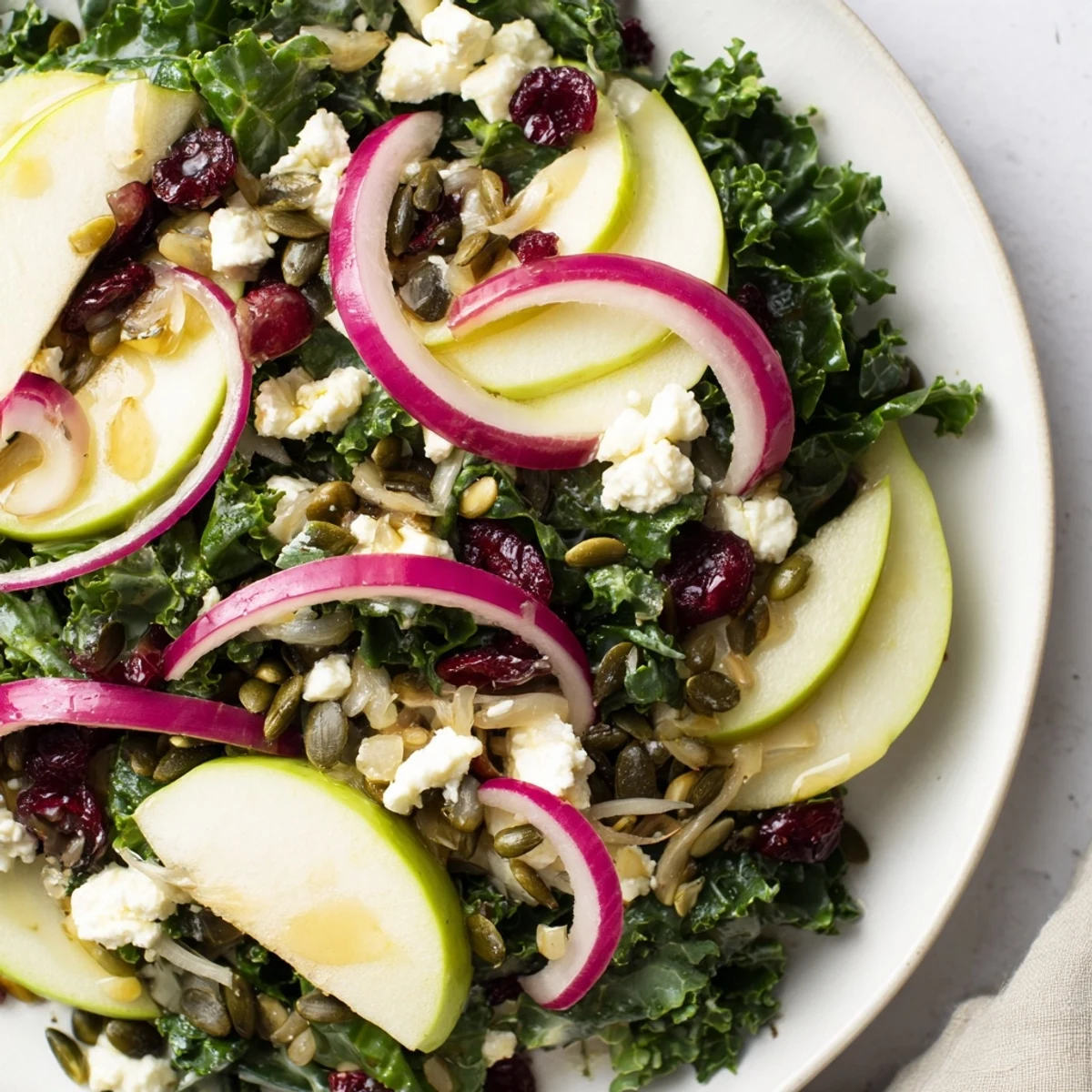 A close-up shows vibrant Winter Kale Salad with Cranberries and Seeds featuring apple slices and a zesty citrus dressing.
