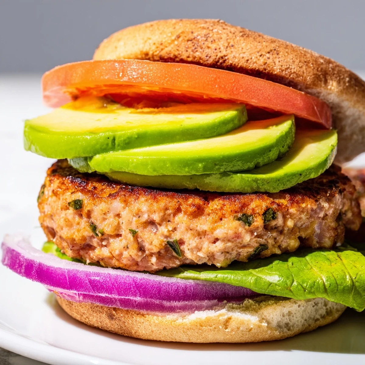 A plated turkey burger with avocado slices layered over crisp lettuce and tomato, perfect for a healthy lunch or dinner.