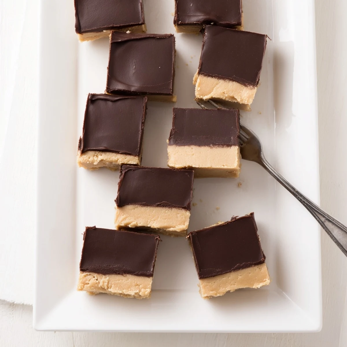 A single piece of Chocolate Peanut Butter Fudge on a dessert plate, garnished with flaky sea salt and chopped peanuts.