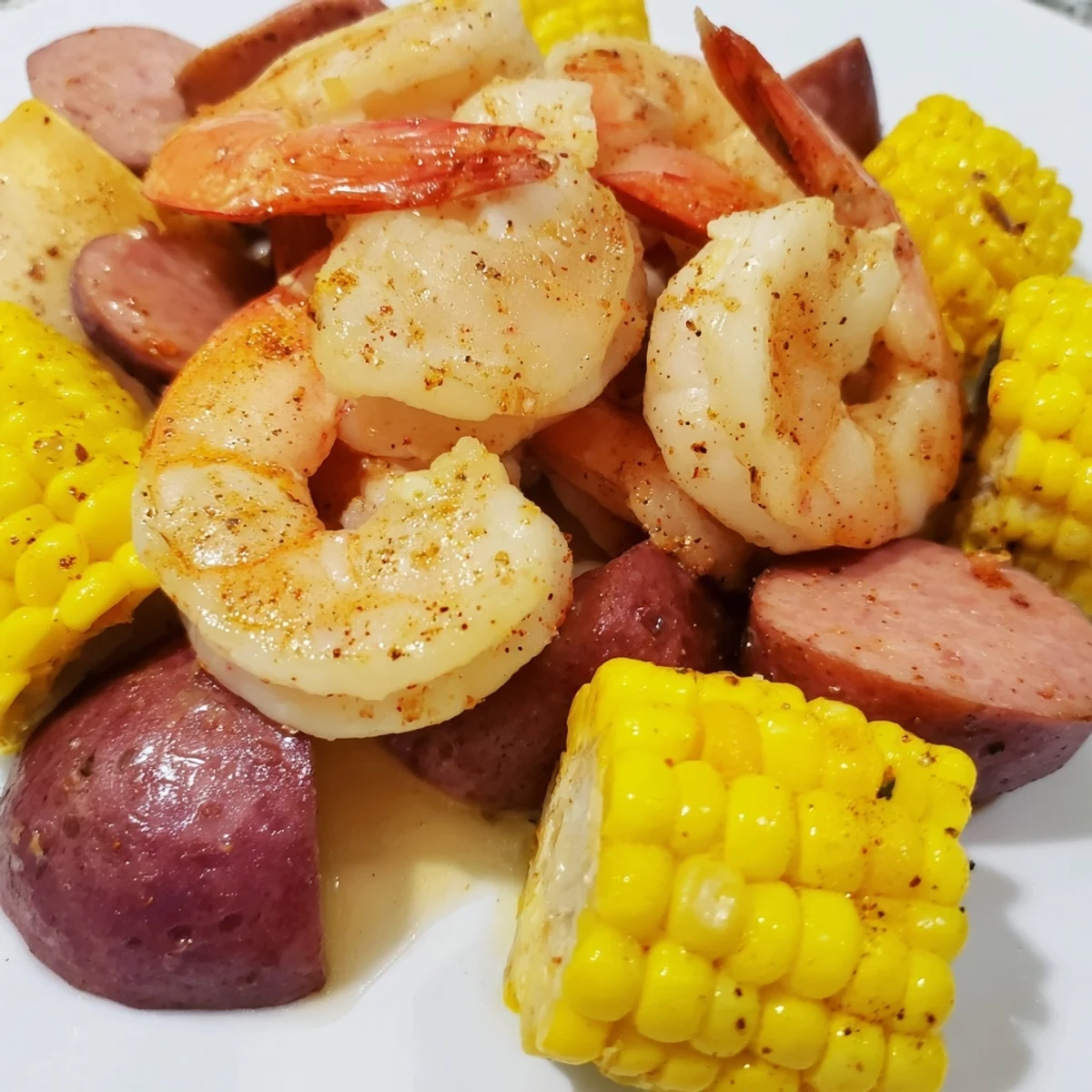 Steaming Creole Seafood Boil featuring shrimp, crab, andouille sausage, potatoes, and corn, drenched in a spicy, aromatic broth and garnished with fresh parsley.  