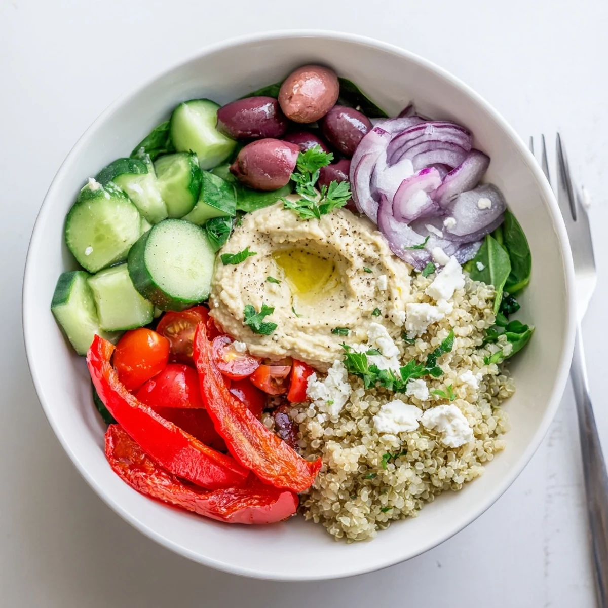 A close-up of a vibrant Mediterranean Quinoa Bowl with Hummus, featuring fluffy quinoa topped with crisp vegetables and a creamy dollop of hummus.