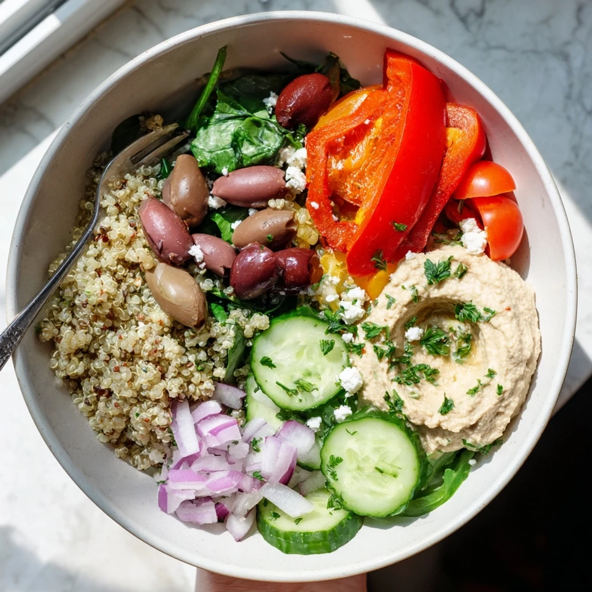 This Mediterranean Quinoa Bowl with Hummus showcases colorful cherry tomatoes, diced cucumber, and crumbled feta with a glossy lemon-tahini dressing.
