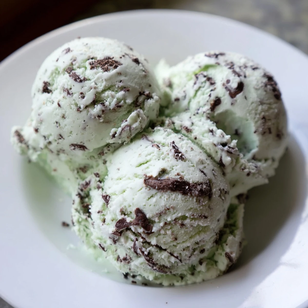 Close-up of homemade Green Mint Chocolate Chip Ice Cream in a bowl, mint flecks visible with rich chocolate chips throughout.