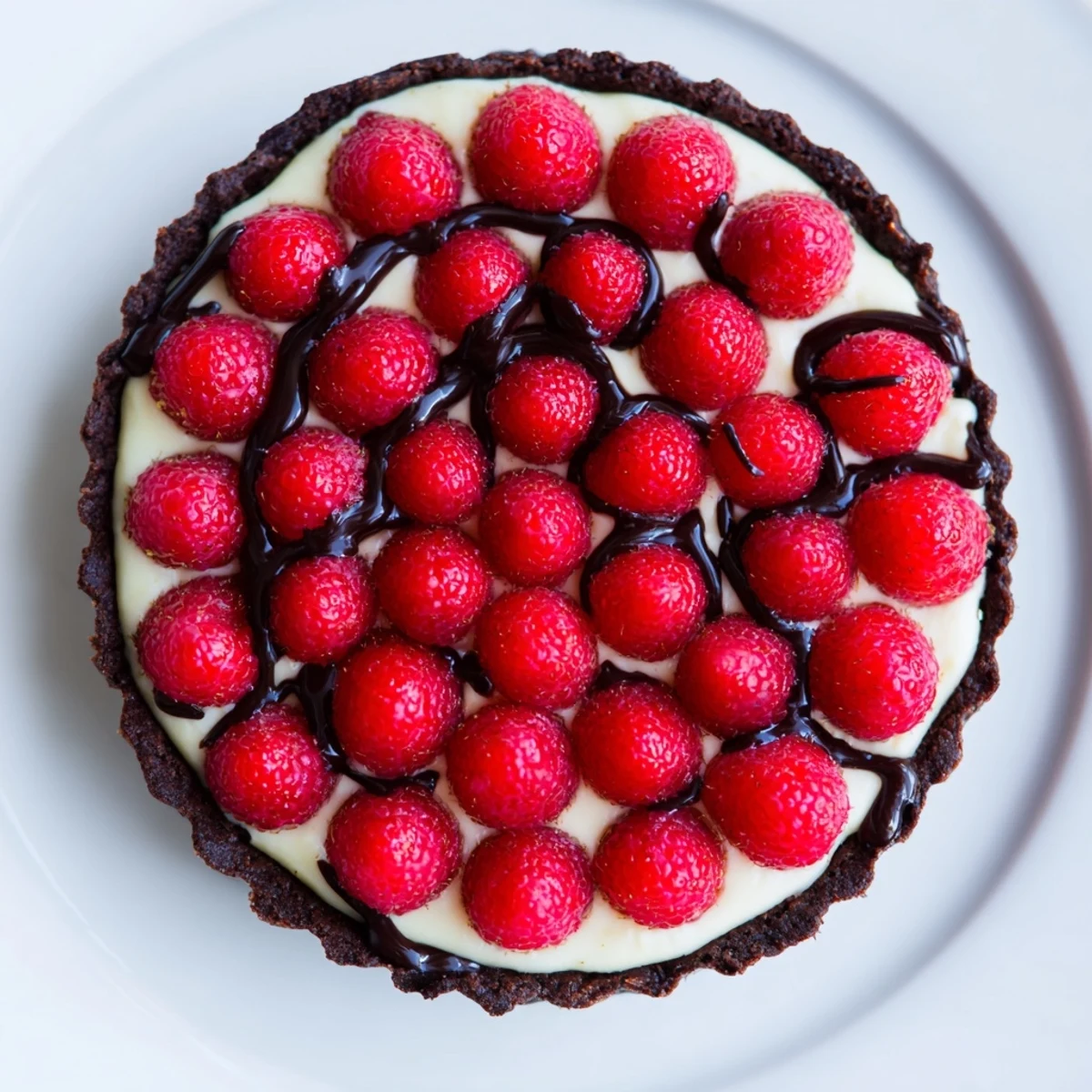 The finished Chocolate Raspberry Tart with Pastry Cream sits sliced on a rustic plate, with a chocolate drizzle.