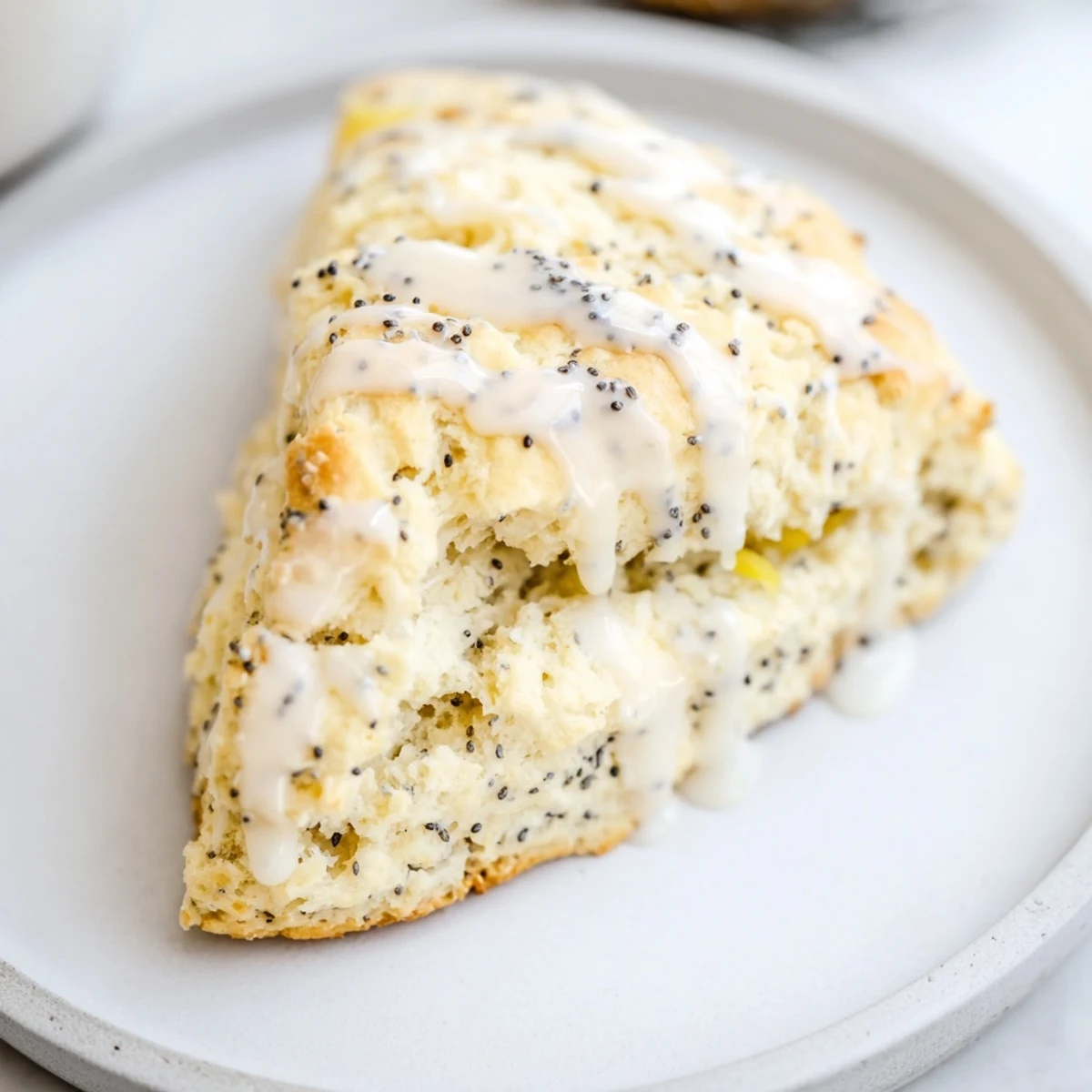 Plated Lemon Poppy Seed Scones are drizzled with sweet glaze, pairing beautifully with a steaming cup of morning coffee.