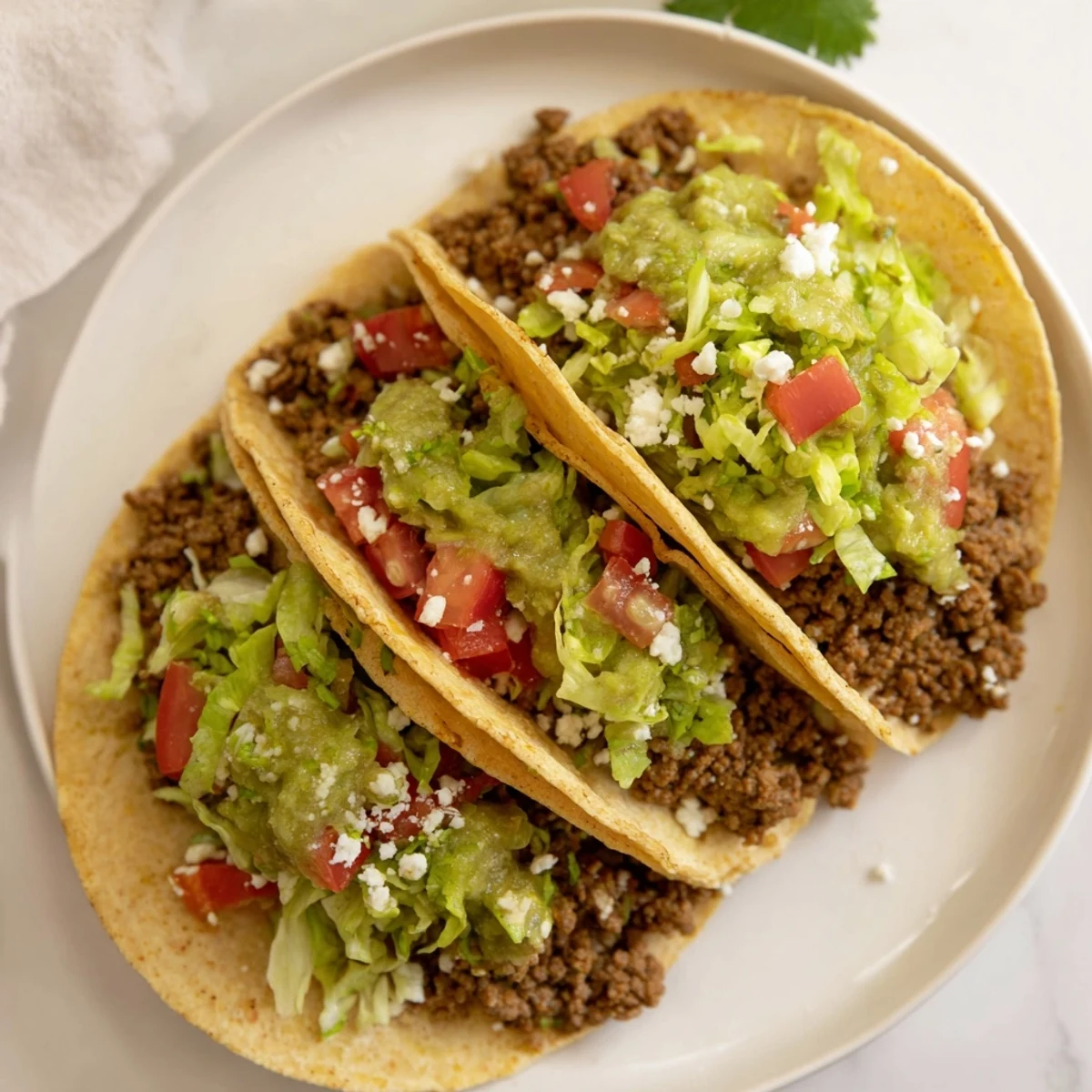 Close-up of spicy beef tacos with salsa verde, diced tomatoes, and jalapeños on a rustic plate.