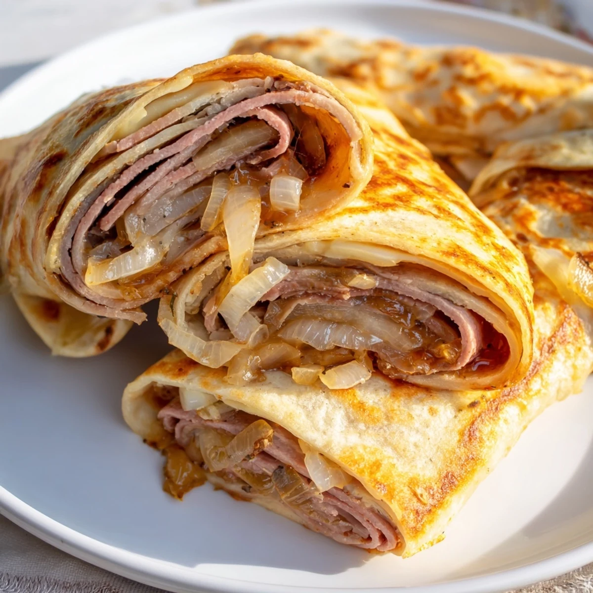 Close-up of Easy French Dip Tortilla Roll Ups showing melted cheese oozing from the ends, with a small ramekin of rich au jus for dipping beside them.