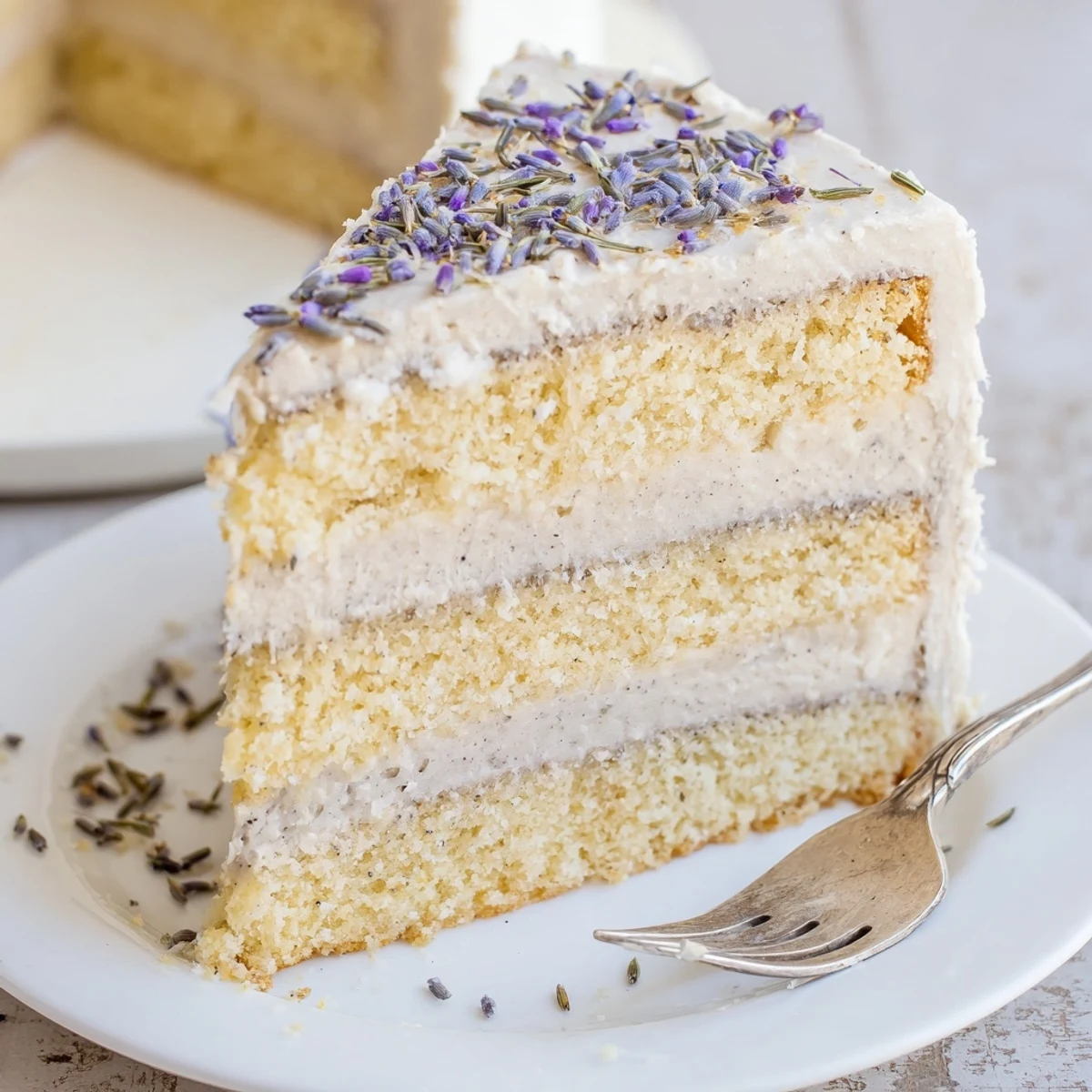 A slice of London Fog Cake with Earl Grey and Lavender next to a steaming cup of tea, perfect for an afternoon treat.