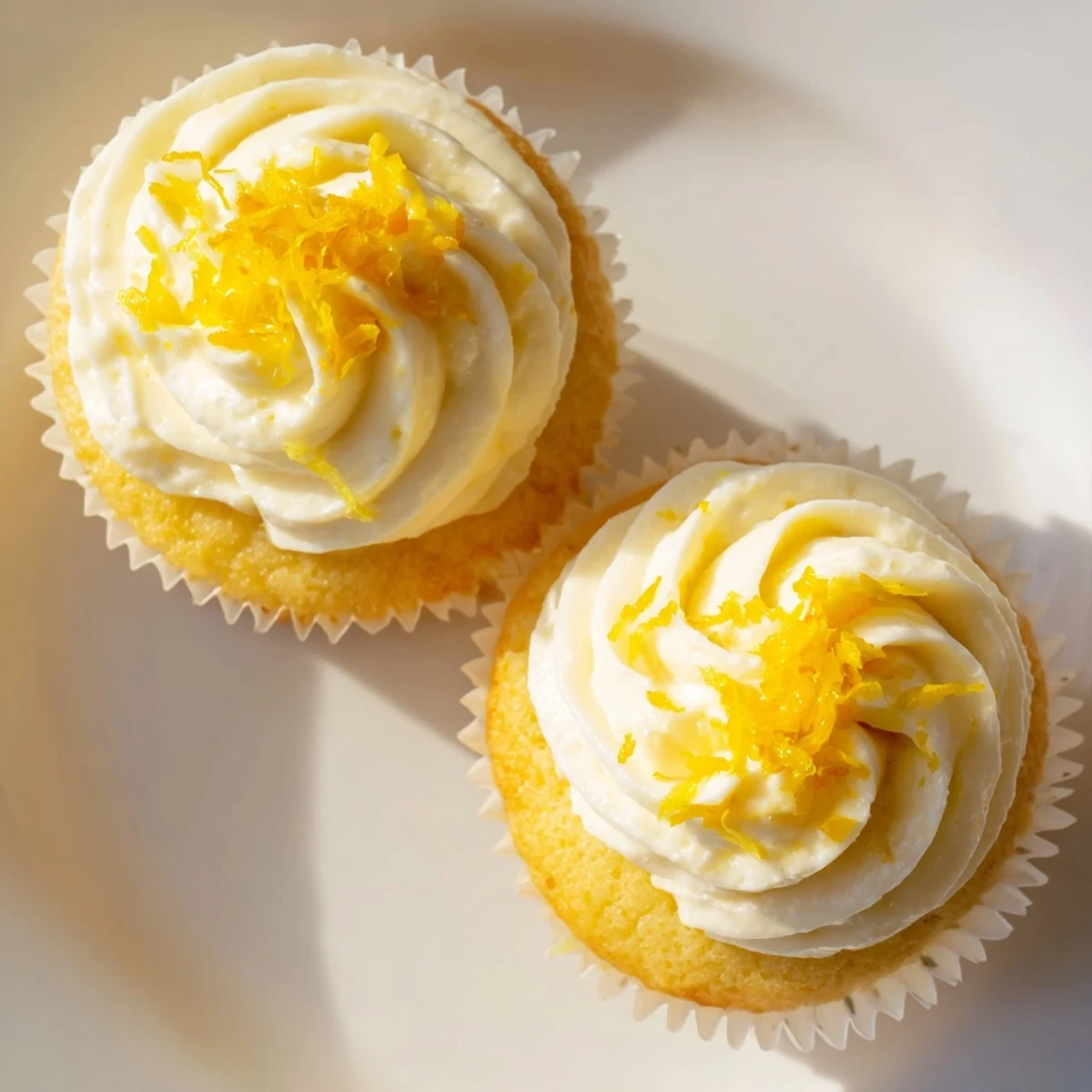 Twelve light and moist Limoncello Cupcakes with creamy frosting and lemon zest garnish, arranged on a white ceramic platter.