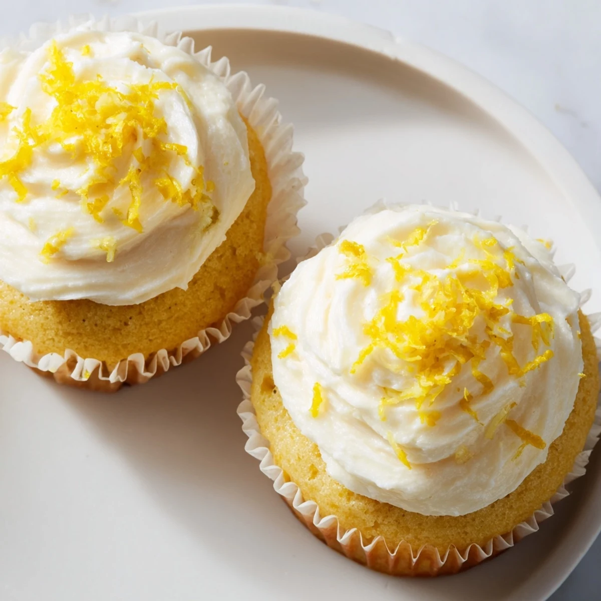 A close-up of a Limoncello Cupcake reveals fluffy frosting and lemon zest topping, ready to serve.