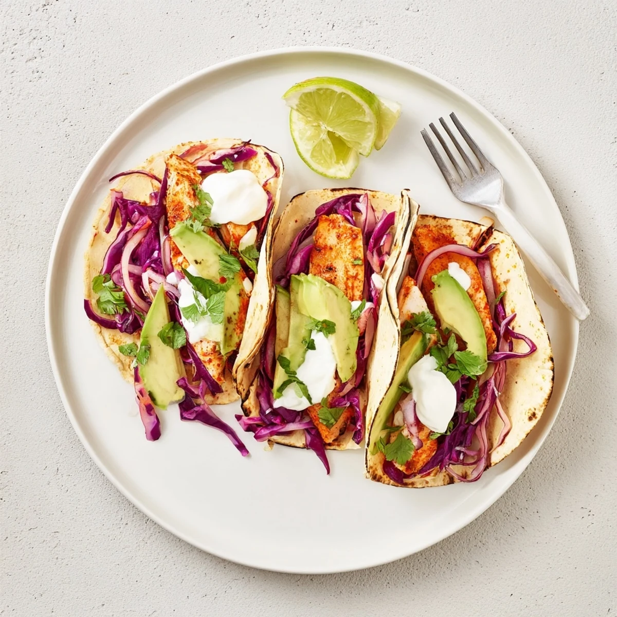 Assembled Aussie Barra Tacos on a plate, featuring zesty slaw, cilantro garnish, and lime wedges for a healthy meal.