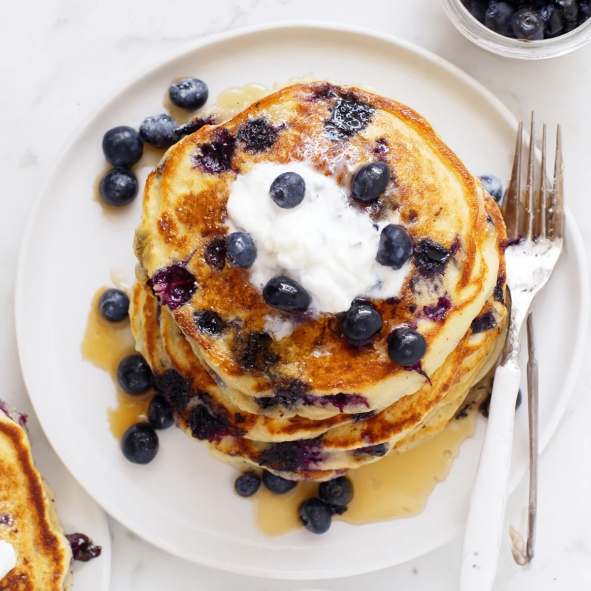 A close-up of Greek Yogurt Blueberry Pancakes cooking on a griddle, bubbling with fresh blueberries and vanilla.