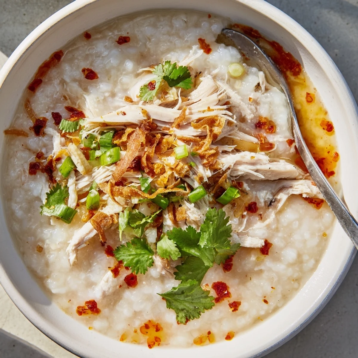 Steaming bowl of Asian fusion turkey congee with shredded holiday meat and garnishes of cilantro and chili oil