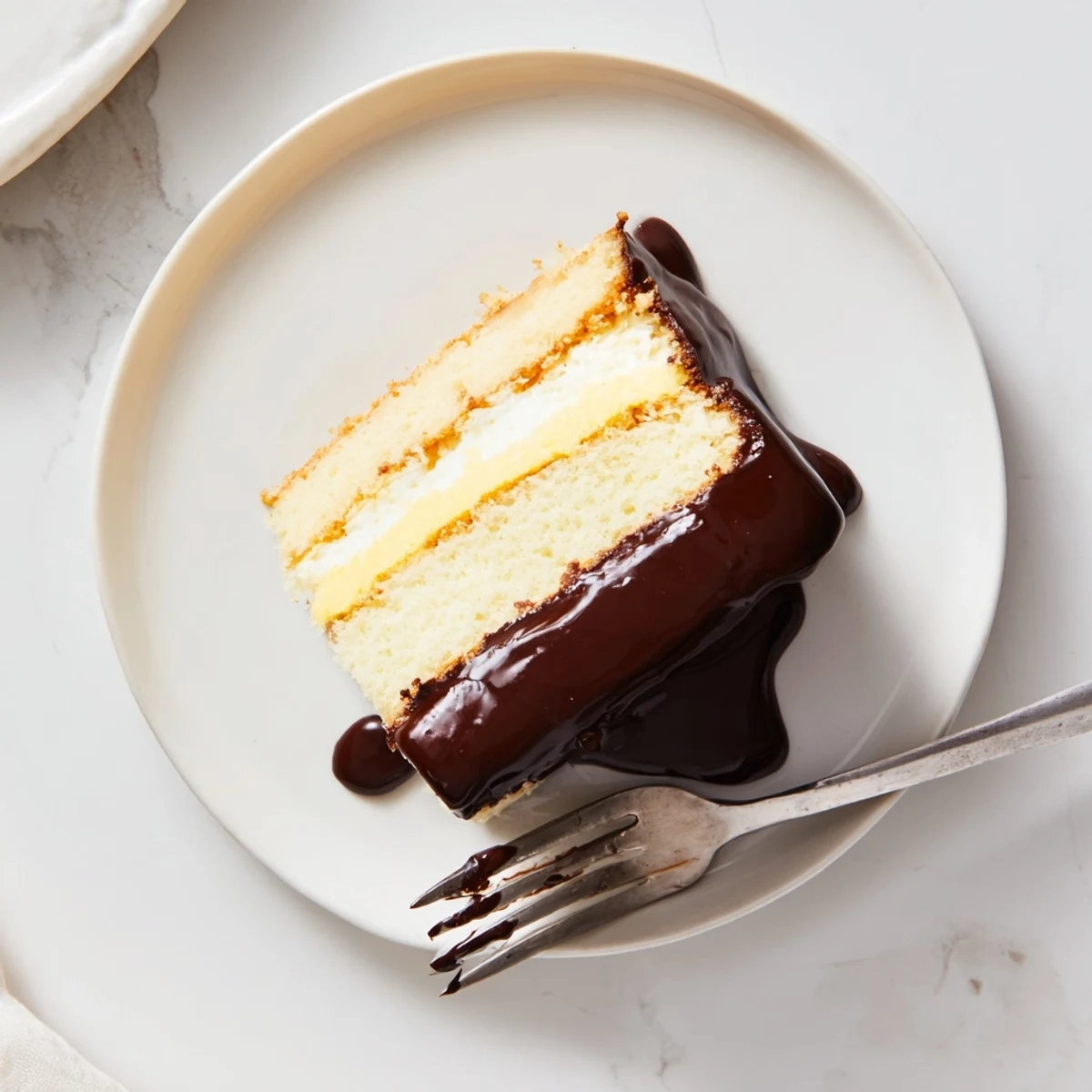 Classic Boston Cream Pie slice revealing vanilla cream and chocolate ganache layers on white plate