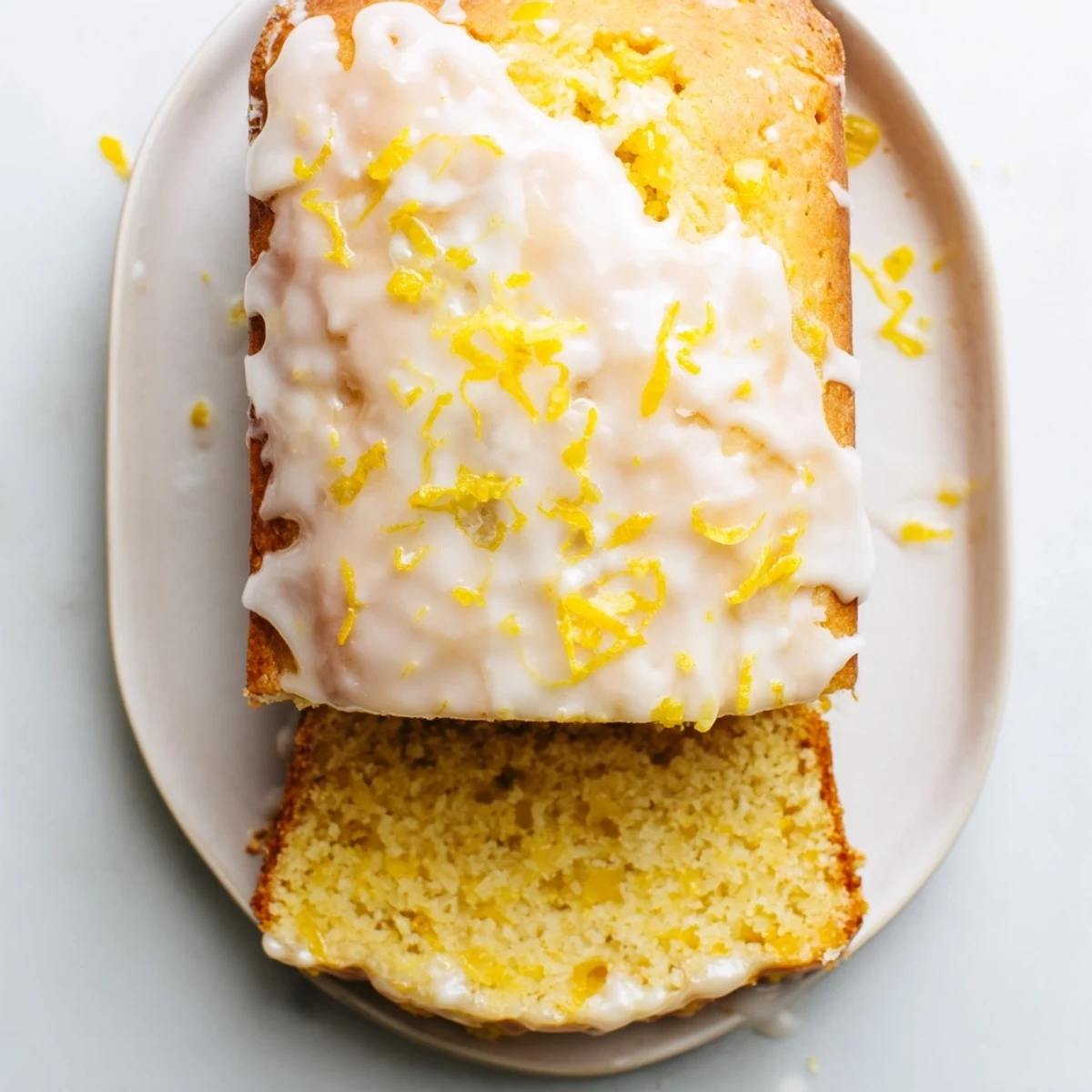 Moist lemon loaf cake with vibrant yellow glaze sliced on a wooden cutting board