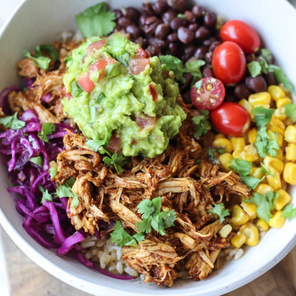 Golden shredded chicken atop fluffy rice with creamy guacamole and colorful fresh vegetables in a vibrant Tex-Mex bowl
