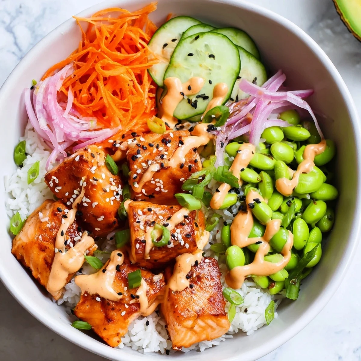 Colorful easy salmon bowl with fluffy rice, avocado, cucumbers, and spicy sriracha mayo drizzle