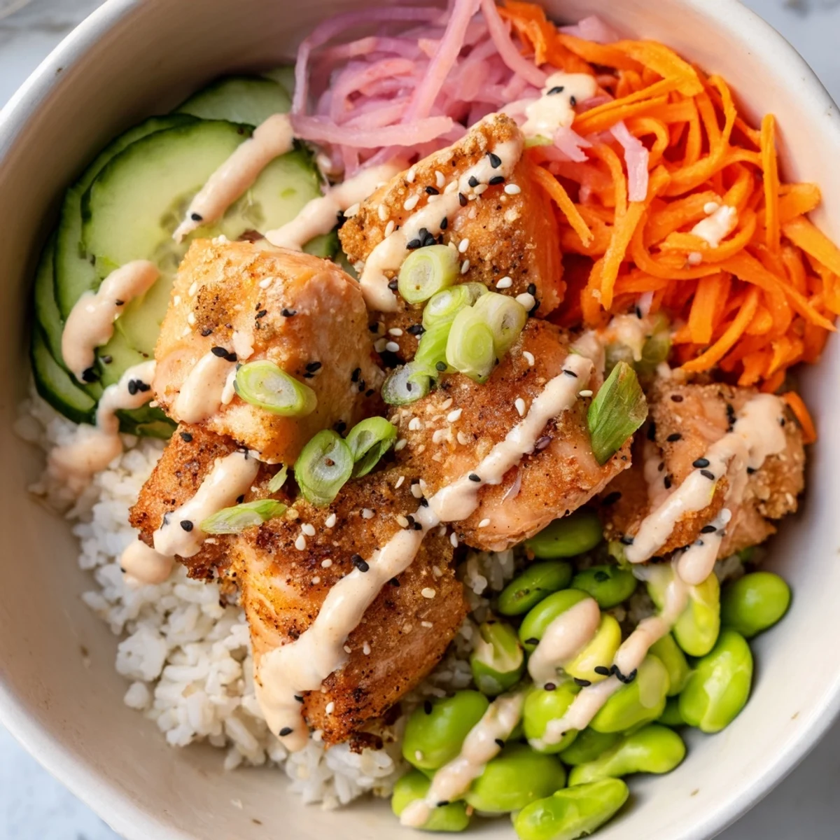 Tender baked salmon pieces over rice bowl with fresh vegetables and zesty creamy sauce topping