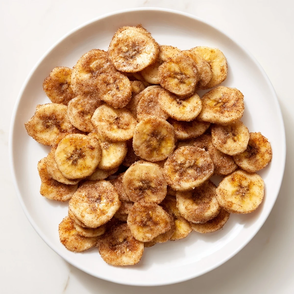 Golden crispy cinnamon sugar banana chips arranged on a white plate with light dusting of spice