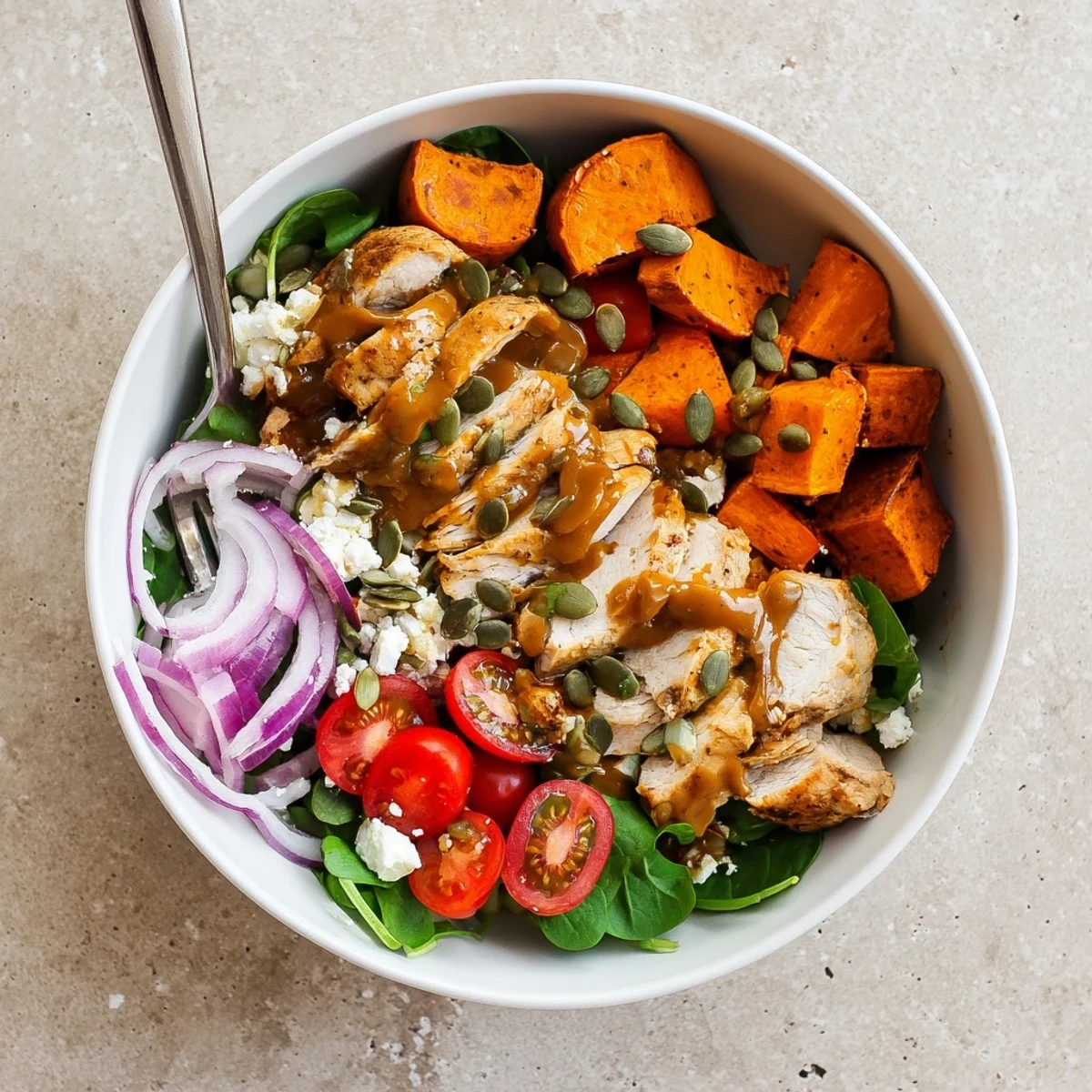 Sliced maple Dijon chicken arranged over caramelized sweet potatoes, cherry tomatoes, and greens in a balanced dinner bowl.