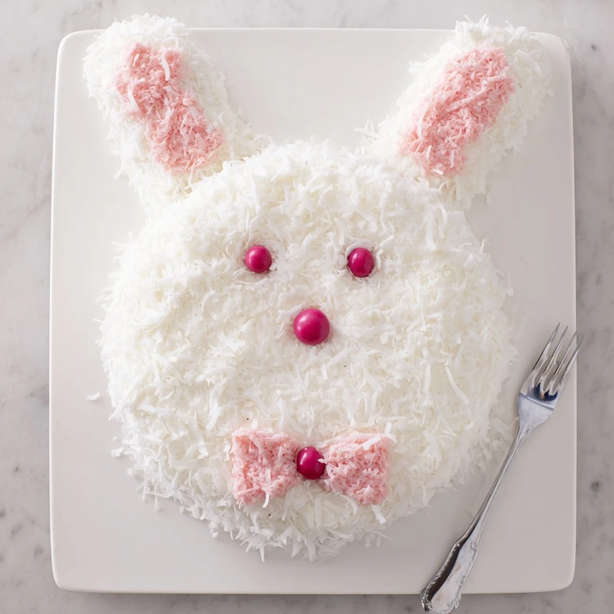 Festive bunny-shaped cake with coconut coating, fondant ears, and jelly bean accents