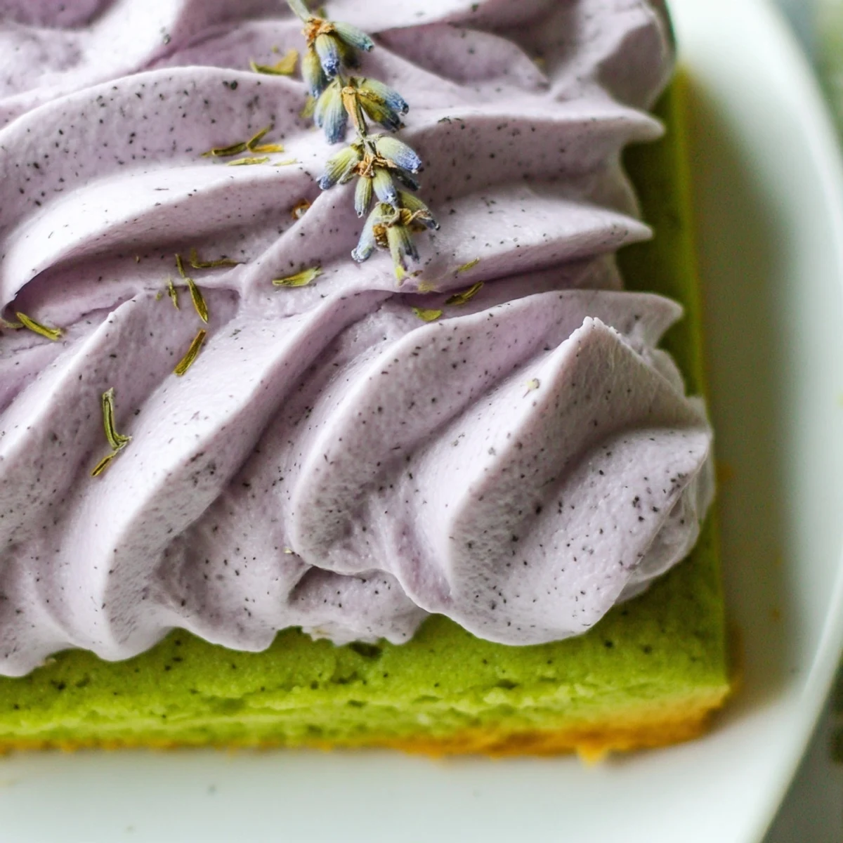 Soft green matcha sugar cookies with swirled lavender frosting on a rustic white ceramic plate