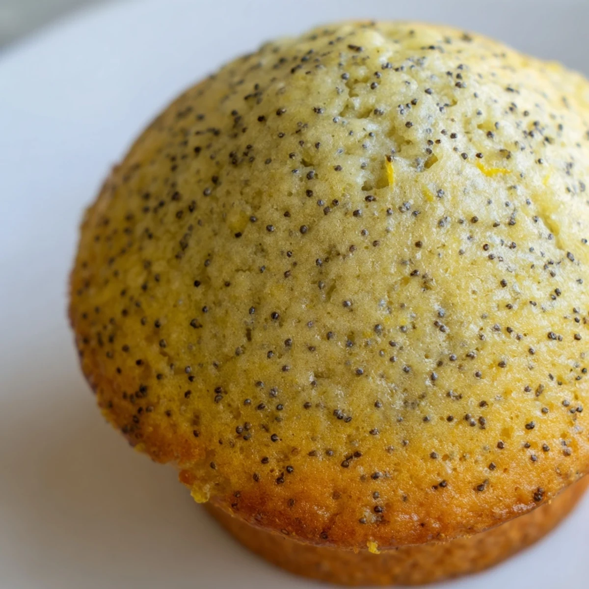 Moist lemon poppy seed muffins studded with tiny black seeds beside a bowl of bright lemon zest