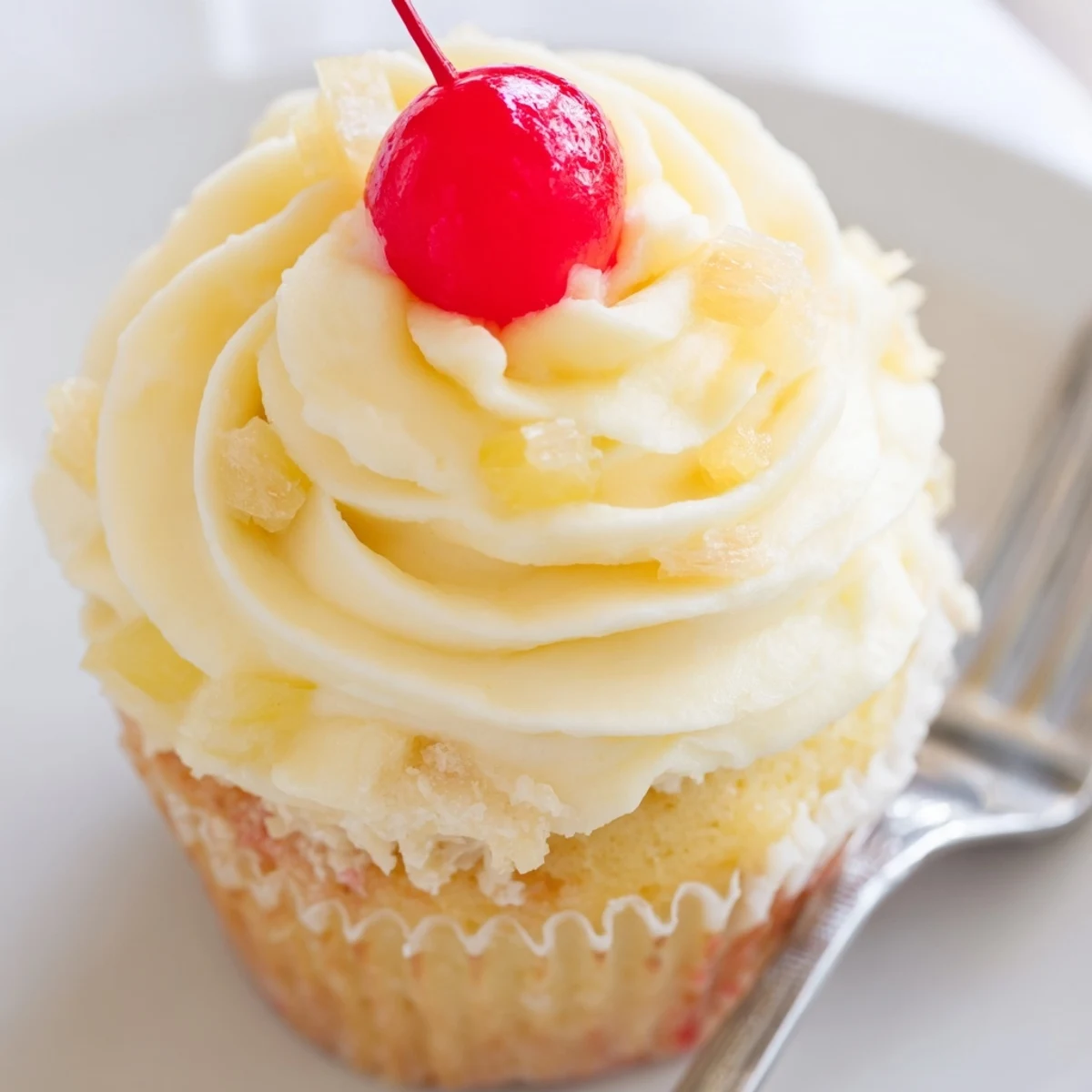 Golden Dole Whip Cupcakes topped with fluffy pineapple cream frosting and cherry garnish