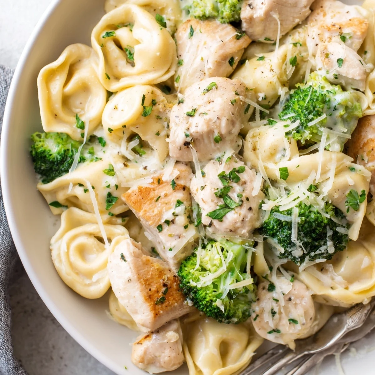Steaming plate of Creamy Garlic Parmesan Tortellini Chicken Broccoli Recipe, garnished with parsley