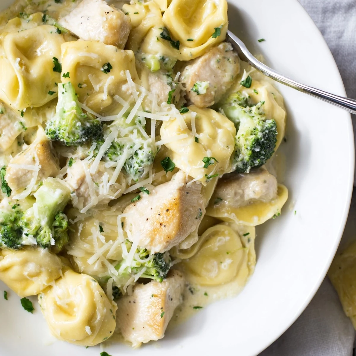 A bowl of Creamy Garlic Parmesan Tortellini Chicken Broccoli Recipe, rich, cheesy sauce