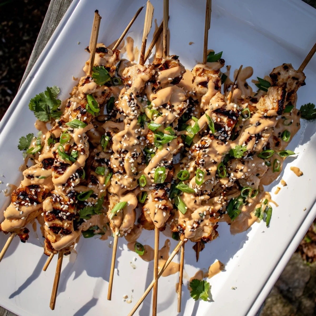 Tender Bang Bang Chicken Skewers on a serving plate brushed with red sriracha dressing