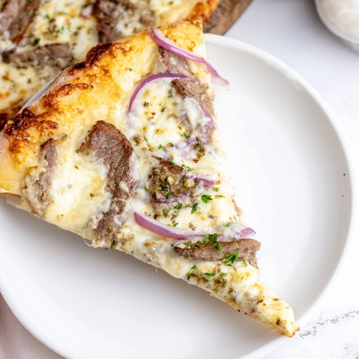 Savory sliced beef atop creamy garlic alfredo sauce with red onion on golden homemade pizza