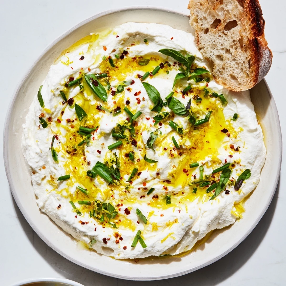 Creamy whipped ricotta spread drizzled with olive oil and topped with fresh herbs on a serving board