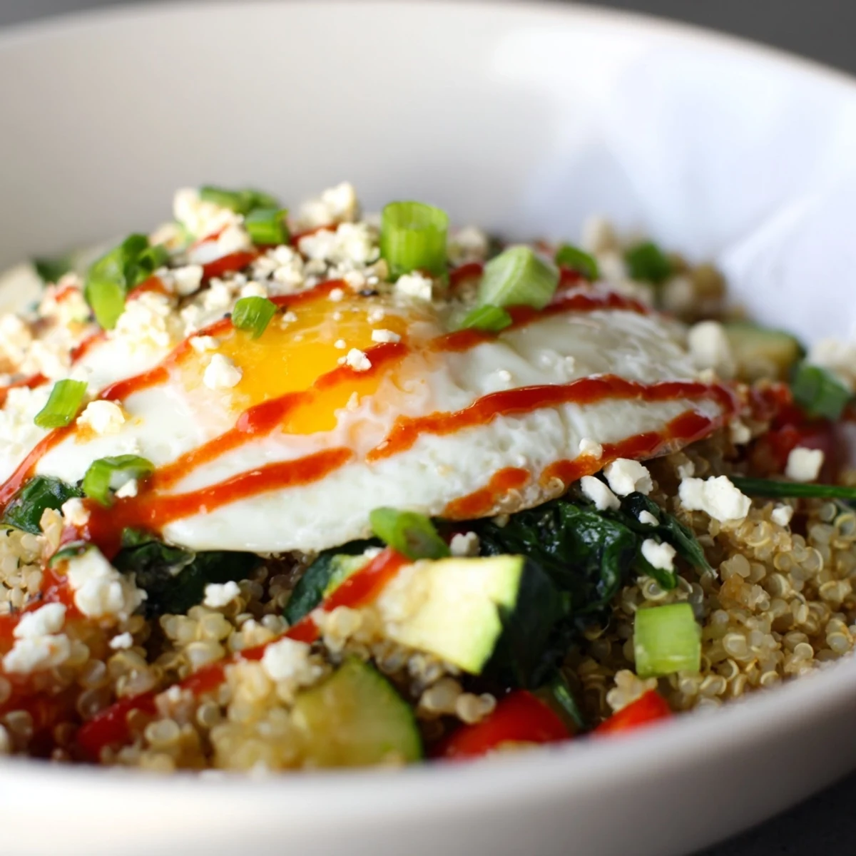 Golden fried egg resting on a savory quinoa breakfast bowl with crumbled feta