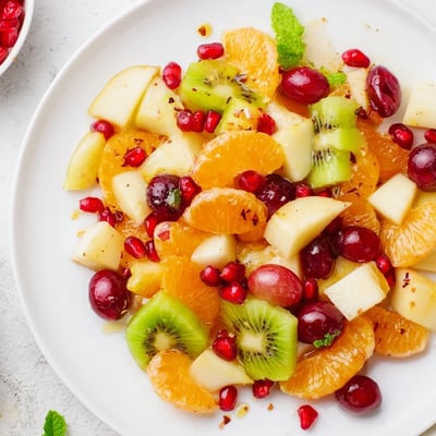 A large bowl of Winter Fruit Salad with Citrus Dressing, loaded with crisp diced apple, juicy pear, and halved red grapes tossed in a glossy honey-ginger coating.