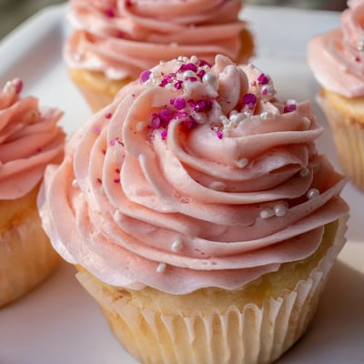 Ten Girl Baby Shower Cupcakes sit on a cooling rack, their soft pastel pink frosting and tiny decorative pearls visible.