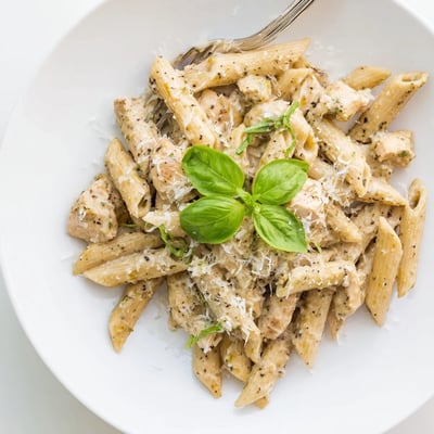 A close-up of Creamy Pesto Chicken Pasta in a white bowl, featuring golden chicken and extra Parmesan on top.