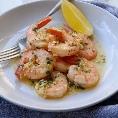 Succulent buttered shrimp sizzling in a rich skillet with minced garlic and lemon wedges